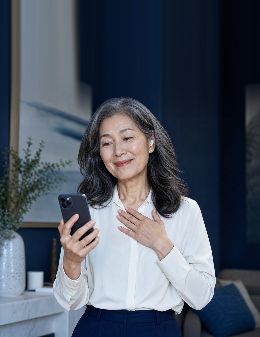A woman listening to a recording on her phone, hand on her heart.